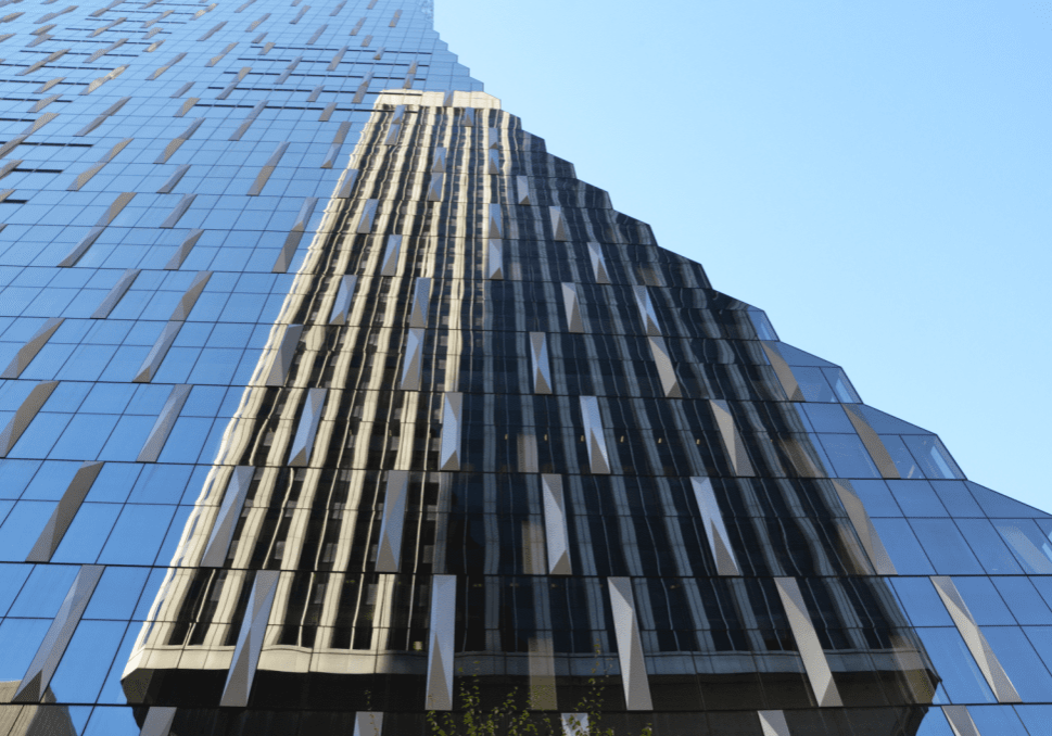 Experience the "Through The Looking Glass Tour" with this architectural close-up of a modern glass skyscraper, its reflective facade shimmering under a clear blue sky.